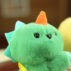 Close-up of green plush dinosaur pendant with orange horns and a yellow ribbon bow