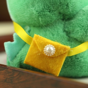 Detail of a plush toy featuring a yellow felt satchel bag with a vintage pearl button