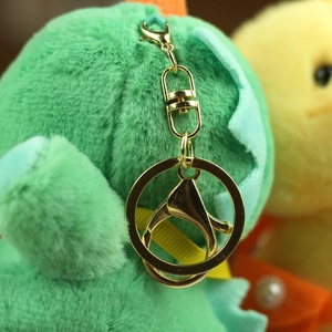 Close-up of green plush dinosaur keychain with golden metal hardware and soft fur texture
