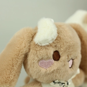 Close-up of soft brown plush bunny with embroidered face details and decorative white ribbon