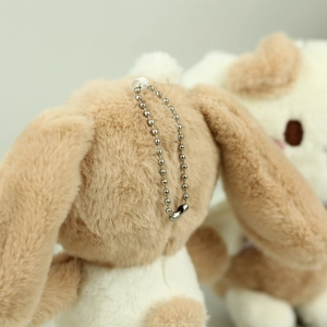 Close-up of plush puppy keychain with silver bead chain and soft white brown fur texture