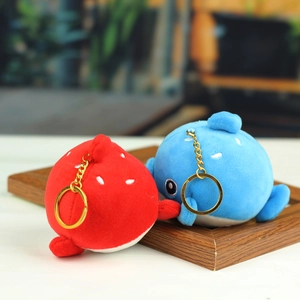 Paire de porte-clés baleines en peluche rouge et bleue sur un plateau en bois naturel