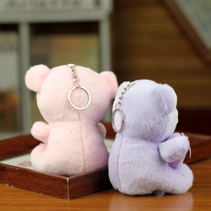 Close-up of pink and purple plush bear keychains with metal rings on a wooden tray