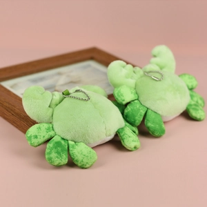 Detail of light green plush crab pendants with silver bead chains on a pink background