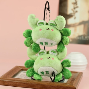 Macro detail of plush green crab keychains with embroidery on a black metal stand