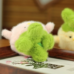 Close-up of pink and green plush chick keychain with metallic clasp on a rustic background