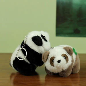Cute plush panda keychains in black and brown with clover leaf on wooden surface