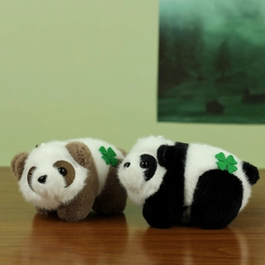 Plush panda keychains in black and brown with green clover embroidery on a wooden surface