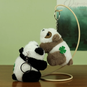 Detail of plush panda keychains in black and brown with clover embroidery and metal rings