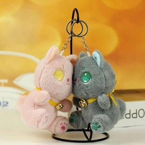 Ricami dettagliati e campanellini dorati su ciondoli a forma di gatto in peluche rosa e grigio