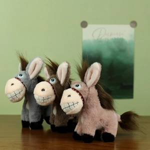 Trois porte-clés ânes en peluche colorés avec de grandes dents sur une table en bois