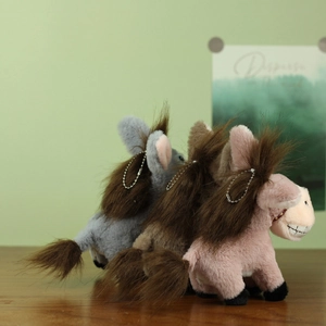 Trois porte-clés âne en peluche en gris, marron et rose sur un bureau en bois