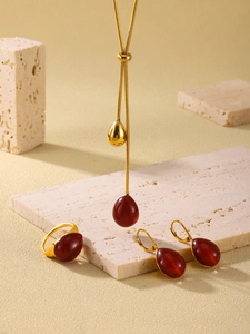 Détail de parure de bijoux dorés avec pendentifs goutte en résine rouge sur pierre texturée