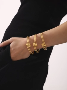 Dettaglio di bracciali a perline placcati oro 18k con terminali a sfera sul polso di una modella