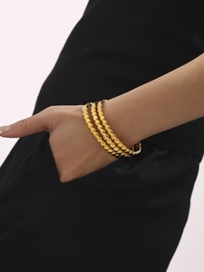 Three-layer gold beaded bracelet worn by model on wrist with elegant high-polish finish