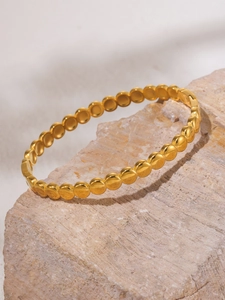 Detailed view of continuous gold dotted disc bangle on a natural stone surface