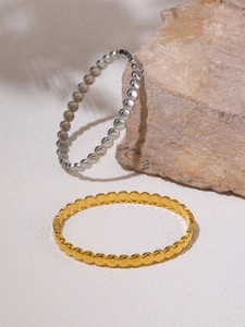 Close-up of gold and silver dotted chain bracelets on a stone and white background