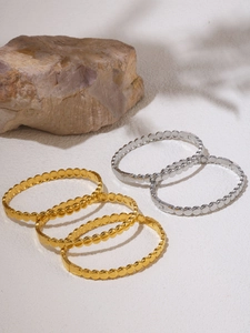 Detailed close-up of 18K gold and silver beaded bangles with stone and leaf shadow
