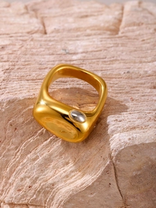Dettaglio anello largo dorato minimalista con accento argento su sfondo di pietra