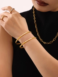 Detail of gold-plated bead bracelets with pearl inlays and paved rings on model