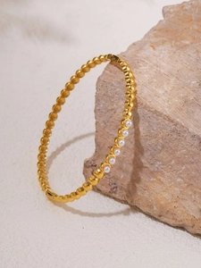 Detailed view of a gold beaded cuff bracelet with six white pearls on stone