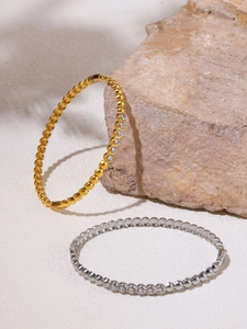 Detail of gold and silver beaded bangles with clear crystals on a textured stone surface