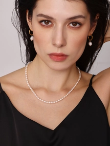Close-up of Baroque freshwater pearl necklace and gold hoop earrings on a female model