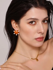 Gros plan d'une boucle d'oreille en émail orange avec perles et collier en chaîne dorée