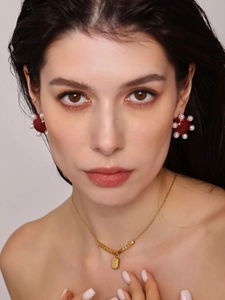 Gros plan de boucles d'oreilles en émail rouge et perles avec collier à pendentif doré