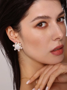 Gros plan d'une boucle d'oreille émaillée blanche avec perles et collier doré sur modèle