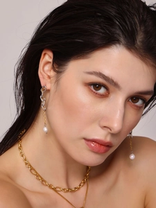 Dettaglio di orecchini a catena con nappa, perle d'acqua dolce e collana d'oro su modella