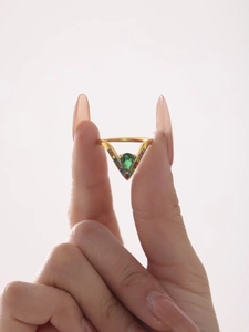 Macro detail of V-shaped gold ring with pear-cut green gem and colorful pavé stones