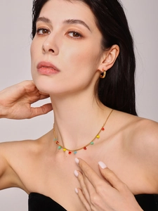 Detail of gold necklace with colorful heart pendants and crystal hoop earrings on a model