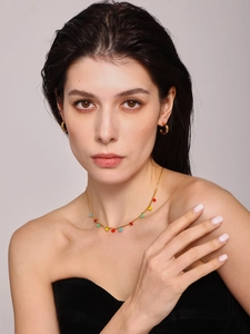 Close-up of golden necklace with colorful heart pendants and zircon hoop earrings on model