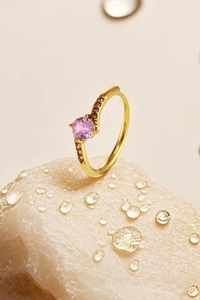 Macro detail of crown ring with pink gemstone and side crystals on gold band