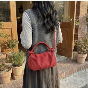 Outdoor shot of a red faux suede dumpling bag with pleated details and shoulder strap