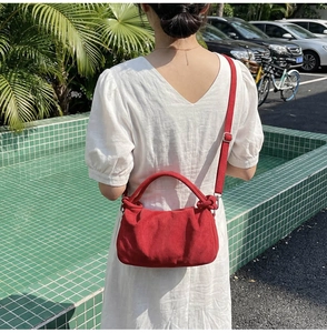 Outdoor shot of a red pleated handbag with knotted detail and adjustable shoulder strap