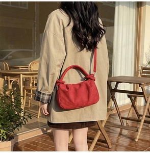 Close-up of a red suede crescent bag with a knotted handle on a trench coat model