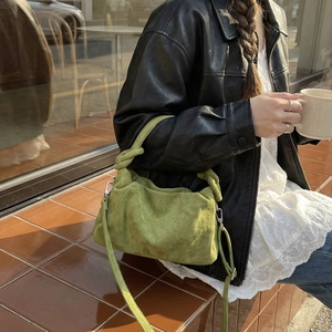 Green suede crossbody bag with knot handle detail shown in a stylish lifestyle setting