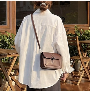 Detail of vintage brown leather crossbody bag with classic metal clasp on cafe background
