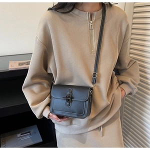 Detail of black leather crossbody bag with white contrast stitching and metal clasp