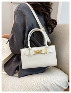 Close-up of a white leather crossbody bag with a heart-shaped golden metal lock detail