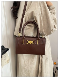 Side view of dark brown tote bag with gold metal buckle on beige trench coat outfit