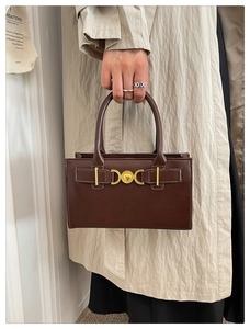 Detail of a dark brown leather handbag with vintage gold buckle held by a person