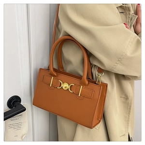 Brown leather crossbody bag with gold heart clasp shown on beige trench coat outfit