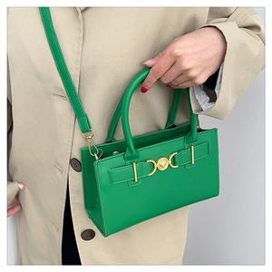 Detail of green handbag with gold heart buckle, shown handheld by a model in a trench coat