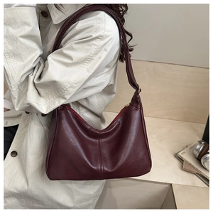 Detail of a dark red leather crescent bag with visible stitching and adjustable strap