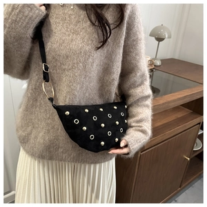 Detail of black suede crescent bag with gold studs and adjustable strap on model