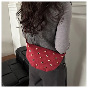 Red suede half-moon shoulder bag featuring golden rivets and metal eyelets on model