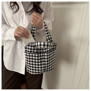 Detail showing a white phone being placed into the side pocket of a checkered canvas tote bag